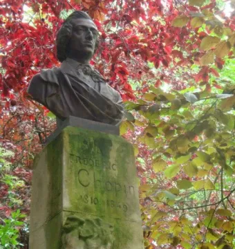 Frederic Chopin bust on a weathered stone column surrounded by autumn leaves.