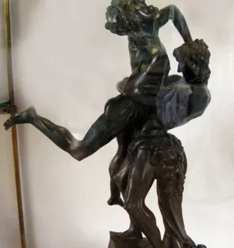 Hercules and Antaeus bronze sculpture showing two muscular figures in a struggle, one lifting the other into the air on a dark pedestal.