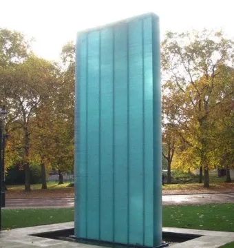 National Police Memorial standing in a shallow dark basin, with light paving, grass, and autumn trees behind it.