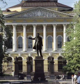 Pushkin statue stands before the Mikhailovsky Palace with a classical facade and trees in the background.