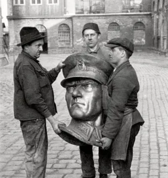 Three workers carrying a large bronze head sculpture of Atatürk in a courtyard.
