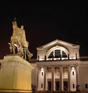 Apotheosis of St. Louis, an illuminated bronze equestrian statue on a tall pedestal in front of a lit classical museum building at night.