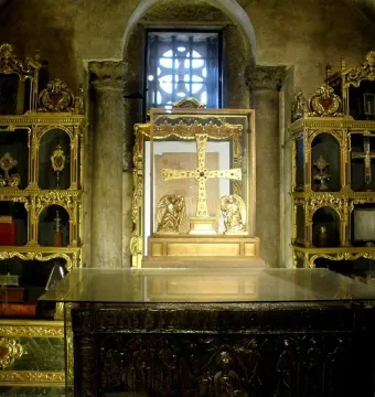 The Cross of the Angels displayed upright in a glass case with two golden figures at its base.