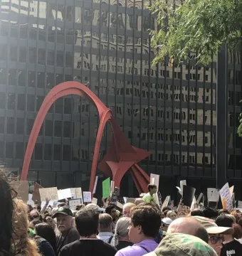 Flamingo sculpture in red steel rising above a crowd in front of a dark building with reflective windows.