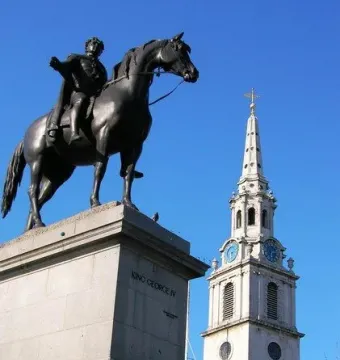 The Equestrian Statue of George IV silhouetted on its pedestal against a blue sky, with a church steeple nearby.