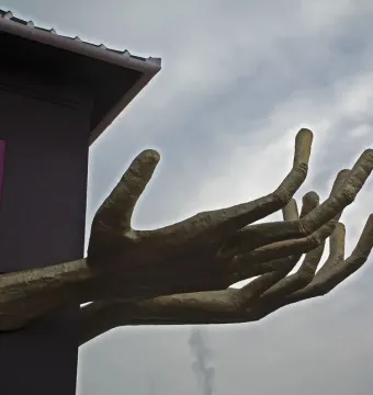 Golden sculptural hands extend from the corner of Kristek House beside a pink-framed window.