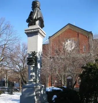 La mort de Dante monument with a dark statue on a tall stone pillar in a snowy park.
