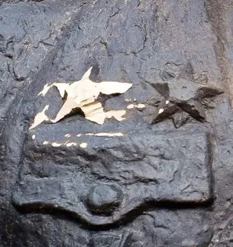 Close-up of the Bronze Soldier showing two embossed star emblems on a dark bronze surface with visible wear.