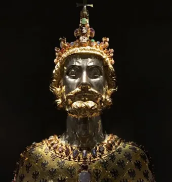 Bust of Charlemagne with a silver-toned face, golden beard, jeweled crown, and ornate gold reliquary chest.