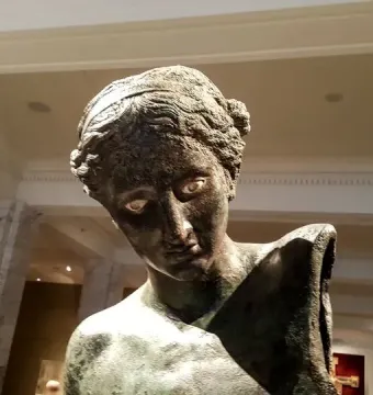 The Cleveland Apollo bronze statue bust with green patina and pale inlaid eyes inside a museum hall.