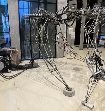 The Senster robotic sculpture with a skeletal metal framework, cables, and jointed limbs beside a separate machinery unit.