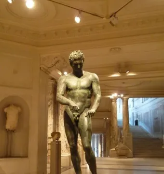 Athlete from Ephesus bronze statue displayed on a pedestal in a grand museum hall.