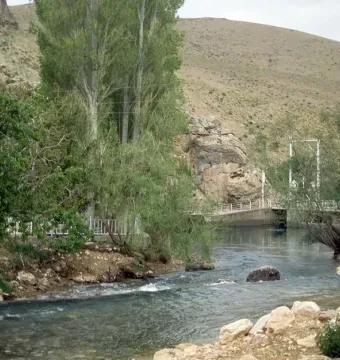 The Ivriz relief carved into a rock face beside the river, with a white railing along the base.