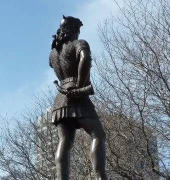Rear view of the Leif Ericson statue in bronze, showing a figure in chainmail and a horned helmet holding a curved horn.