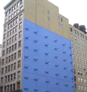 The Wall sculpture on a bright blue building facade with rows of teal projections above a beige lower section.