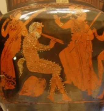 Red-figure ceramic vase showing a seated satyr playing a double flute, with other figures around him.