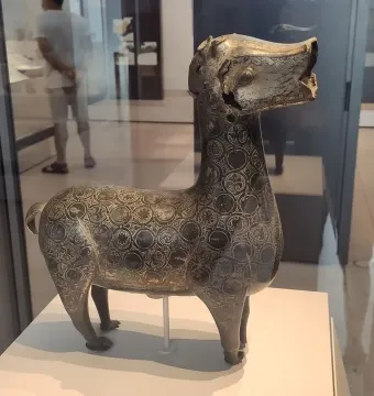 Ciervo de Madinat al Zahra, a bronze-colored deer sculpture with circular patterns, displayed in a museum case.