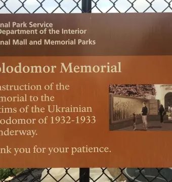 National Park Service sign about Holodomor Memorial construction on a chain-link fence