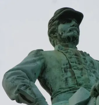 Weathered bronze statue of Major General George B. McClellan in military uniform and cap, seen from below with one hand on his hip.
