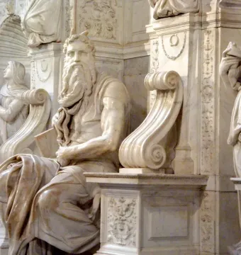 Marble sculpture of Moses seated with tablets, shown with a bearded face and horn-like protrusions.