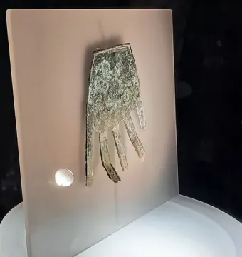 The Hand of Irulegi metal artifact displayed behind glass on a light panel.