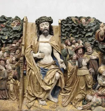 Detail of The Last Judgement sculpture showing a crowned figure amid carved figures, with a bearded figure raising a hand beside kneeling observers and cloud forms above.