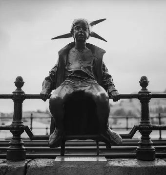 The Little Princess statue sits on a decorative railing, shown in black and white with a distant landscape behind it.