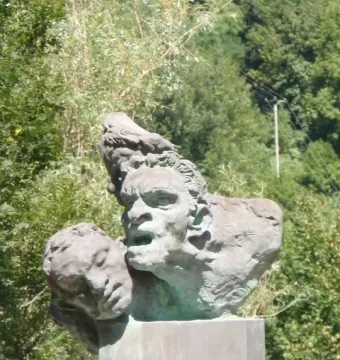 War Memorial of Capoulet-et-Junac with a weathered stone cluster of anguished faces on a concrete pedestal.