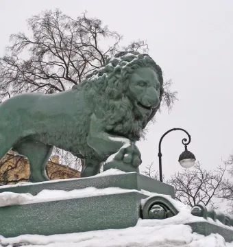 Lions at the Dvortsovaya Pier lion statue with a paw on a sphere, standing on a snow-covered pedestal.