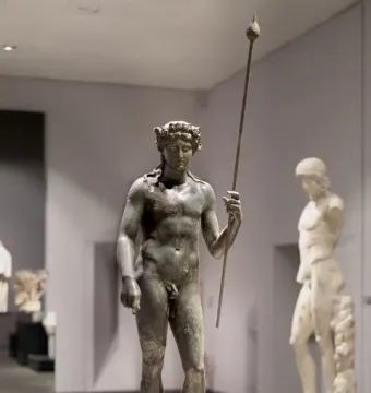 Tiber Dionysus bronze statue of a standing nude male figure with a wreath and staff in a museum.
