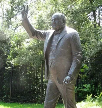Winston Churchill statue making a V-for-Victory sign with one hand and holding a cane.