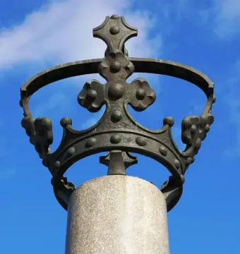Electio Viritim Monument bronze crown on a stone pillar against a blue sky.