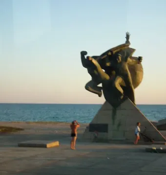 Monument to the Eupatoria Assault, a dark bronze sculpture of three figures on a tall stone pedestal by the sea.