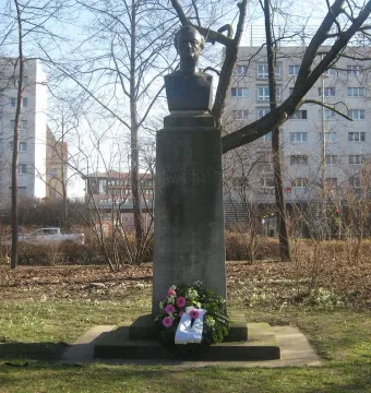 Richard Wagner bust on a tall stone pedestal in a park, with a floral wreath at the base.