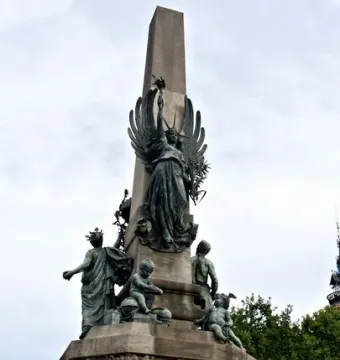 Rius i Taulet Monument with a tall stone pillar, bronze figures, and winged angels on an ornate base.