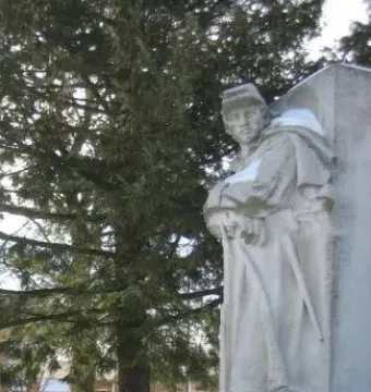 Soldiers\' Monument stone soldier sculpture on a snowy platform beside a wall, with an evergreen tree in the background.