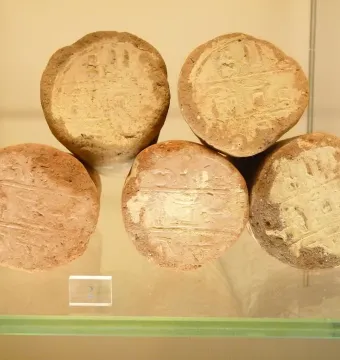 Five terracotta funerary cones with worn impressed inscriptions, displayed on a glass surface.