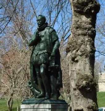 Bronze statue of William the Silent on a stone pedestal, partly obscured by a tree trunk.