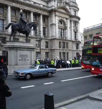 The Duke of Cambridge equestrian statue on a stone plinth in front of a classical building, with traffic and pedestrians nearby.