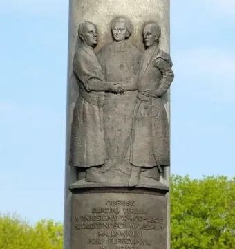 Electio Viritim Monument in Warsaw with a bronze plaque below a relief of three historical figures.