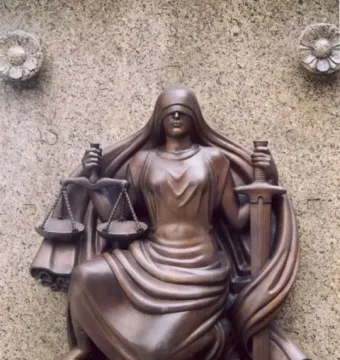 Bronze relief sculpture of Lady Justice seated with scales and a sword on a stone wall.
