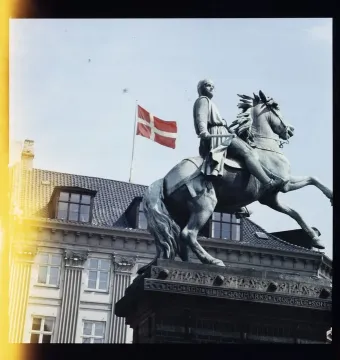 The Absalon Monument, a bronze equestrian statue of a helmeted figure on a rearing horse, stands before a building with a Danish flag.