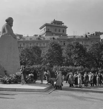 Karl Marx monument with flowers at its base, surrounded by a crowd of people in a black-and-white photograph.