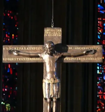 Mindener Cross bronze crucifix with Latin inscriptions and stained-glass windows in the background
