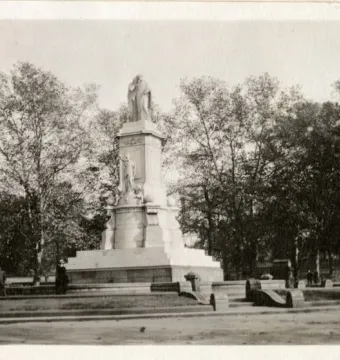 Peace Monument with sculpted figures and a statue at the top, standing among trees in a park-like setting.