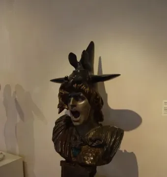 Bronze bust of Bellona with an anguished expression, wearing a helmet and ornate armor with a blue jewel.