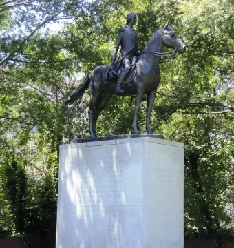 Bernardo de Gálvez equestrian statue on a tall stone pedestal surrounded by trees.