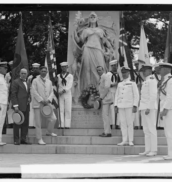 Commodore John Barry statue monument with men gathered on the steps and flags around it.