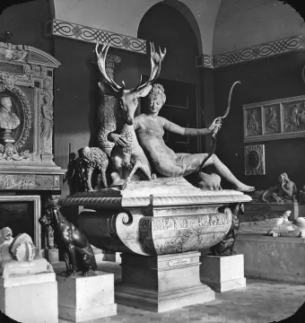 Black-and-white photograph of Diana with a stag sculpture, showing a reclining female figure beside a deer with large antlers in an interior gallery.