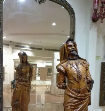 Mephistopheles and Margaretta wooden sculpture showing a bearded male figure, with the female side visible in the mirror behind it.